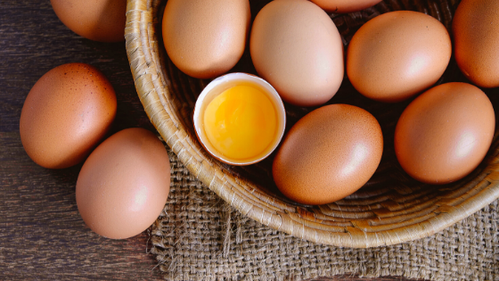 Brown farm eggs on a table. Most are in a basket but two are sitting next to it